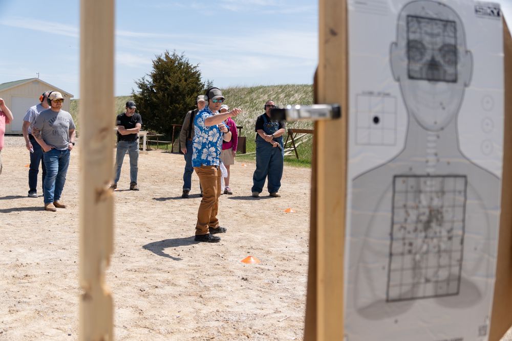 Outdoor shooting range training session with participants observing a shooter, human silhouette target in foreground.