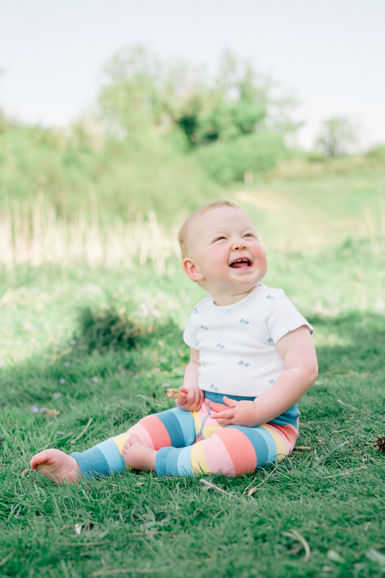 Natural family photography of a baby sitting on grass outdoors, captured during a relaxed documentary family photoshoot