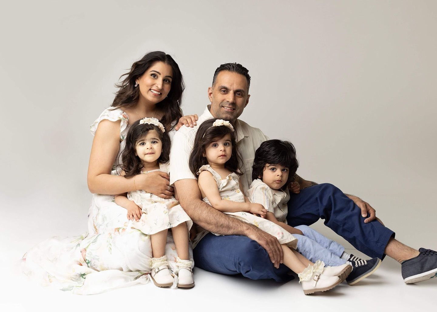 A family sits together on the floor wearing coordinated white and blue outfits for a studio portrait.