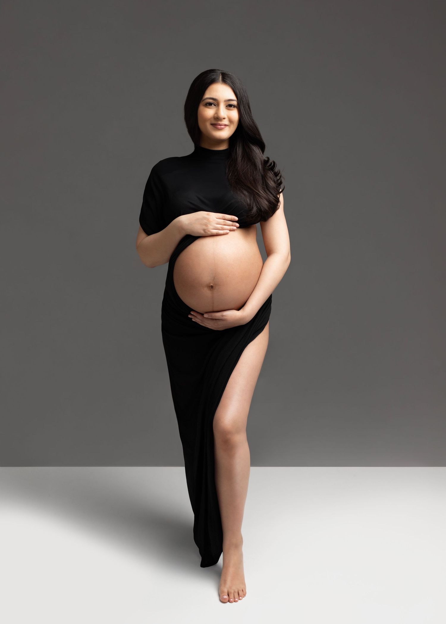 A series of maternity photos showing a woman in black against a gray backdrop posing to highlight her pregnancy.