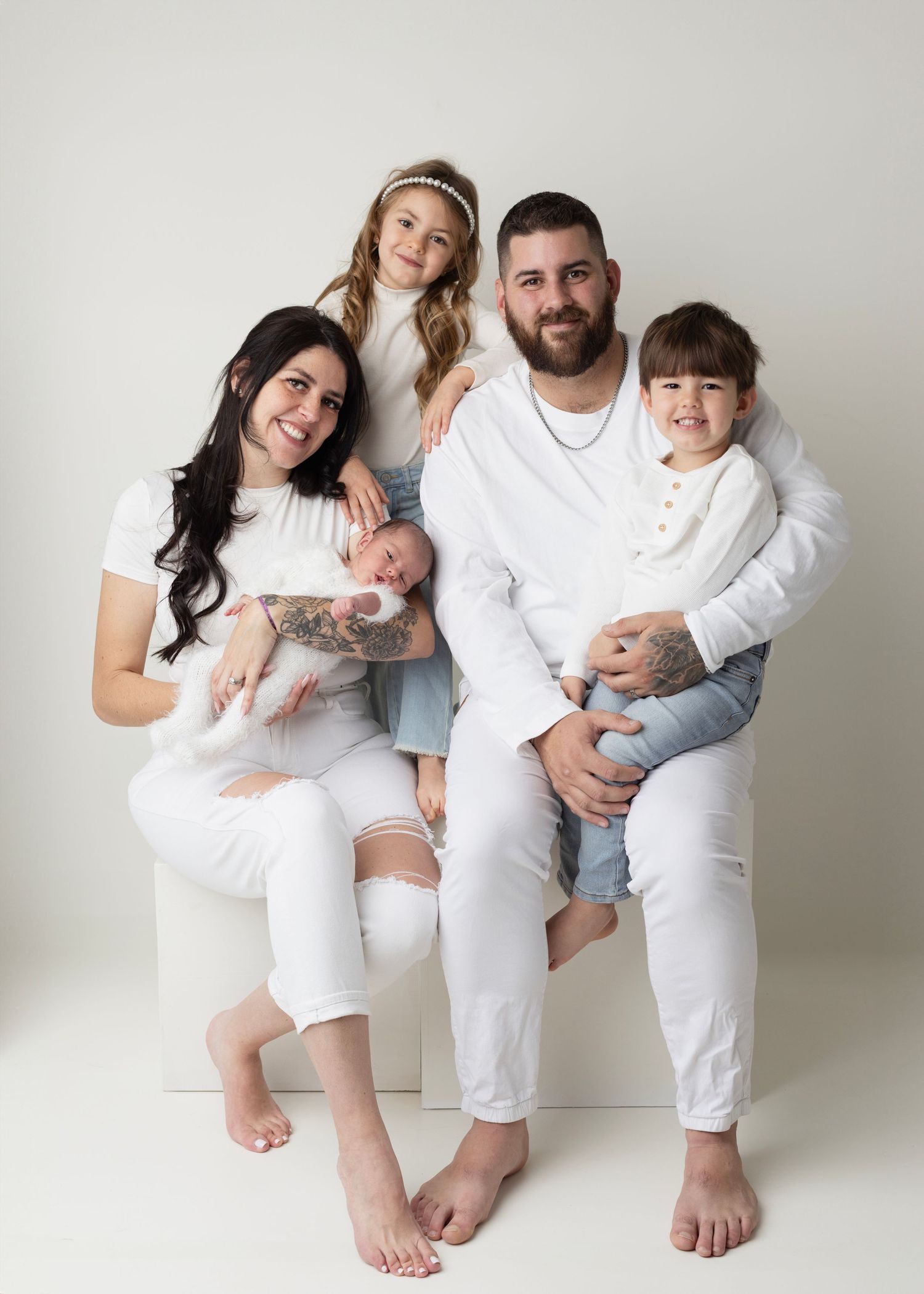 A family of five wearing white outfits poses together for a studio portrait against a light gray background.