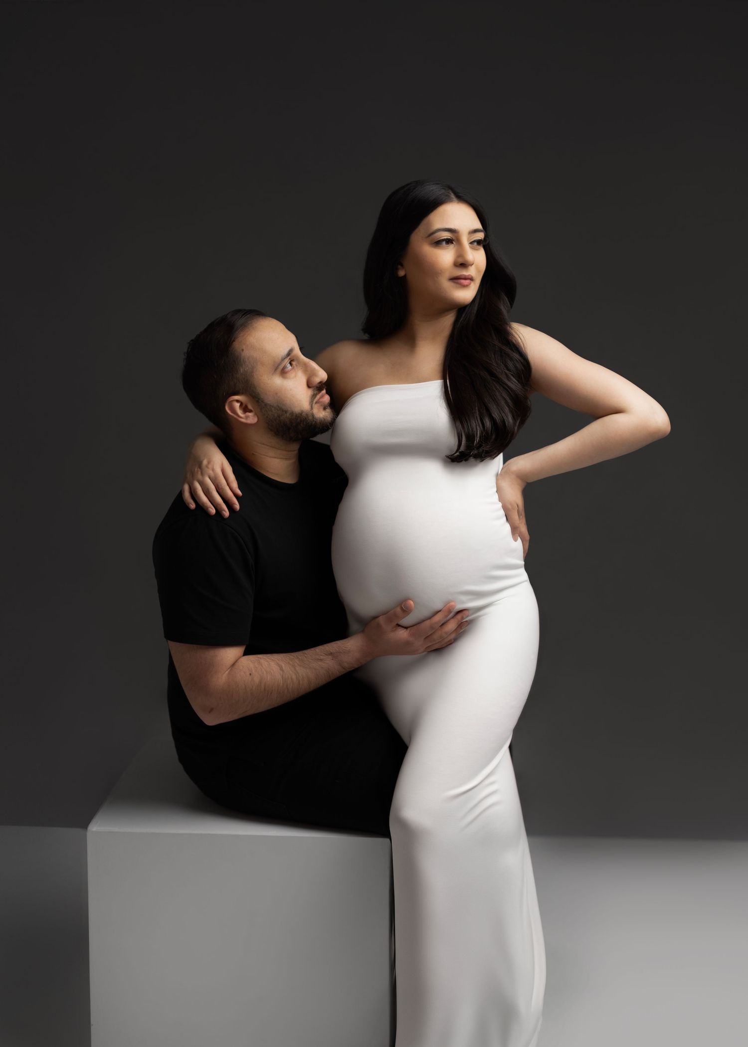 A dramatic black and white maternity photo series showing intimate poses between a couple against a dark background.