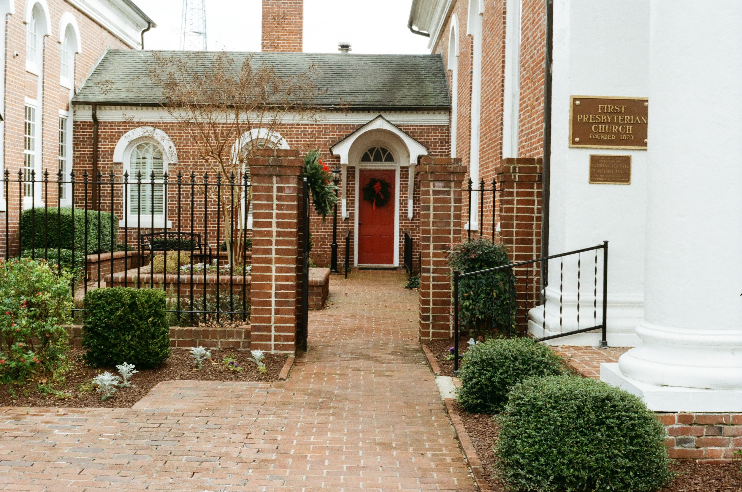A series of brick archways and iron gates leading to a church courtyard with manicured landscaping.