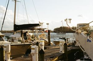 Row of sailboats docked at a marina with mountains visible in the background on a cloudy day.