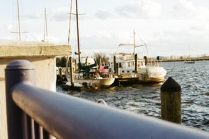 Boats docked at a marina with wooden piers and power lines visible against a cloudy sky.