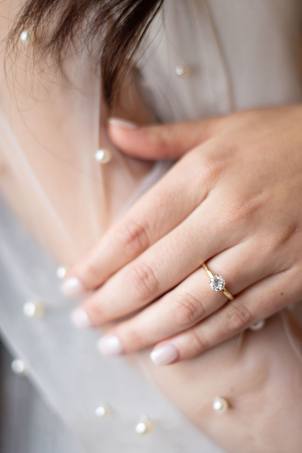 Close-up of delicate pearl details and engagement ring on hands.
