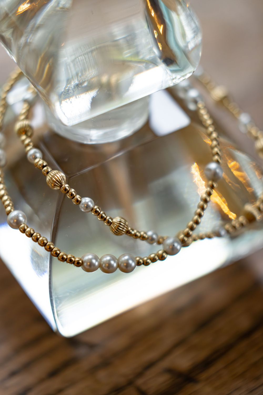 Close-up of delicate gold and pearl jewelry details on a wooden surface.