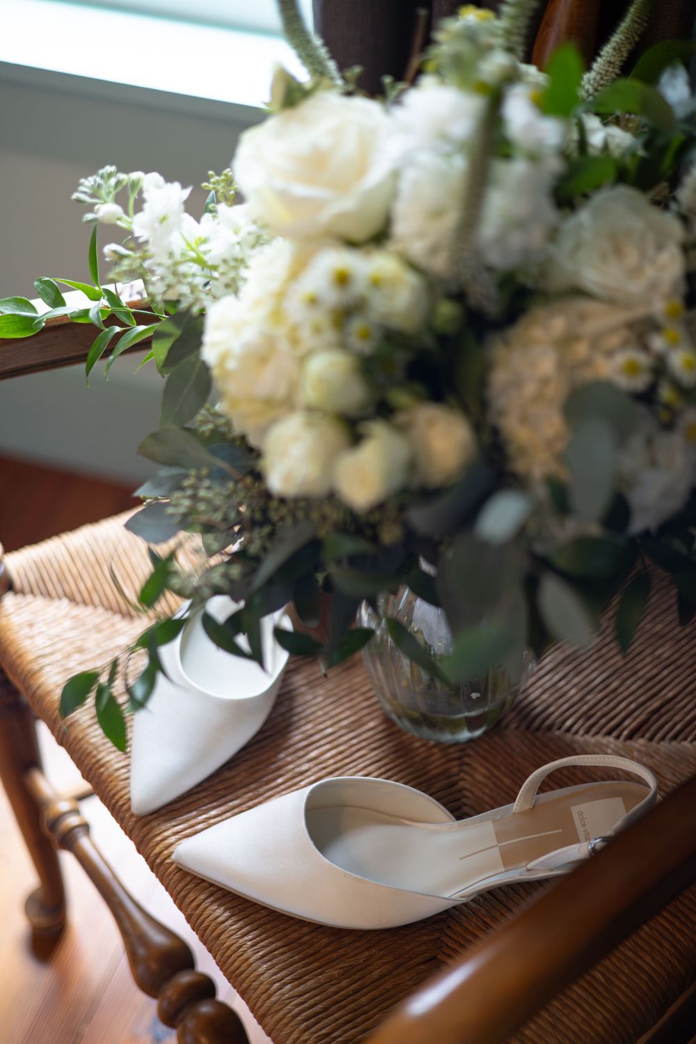 White floral centerpieces in glass vases arranged on a rustic wooden table with elegant place settings.