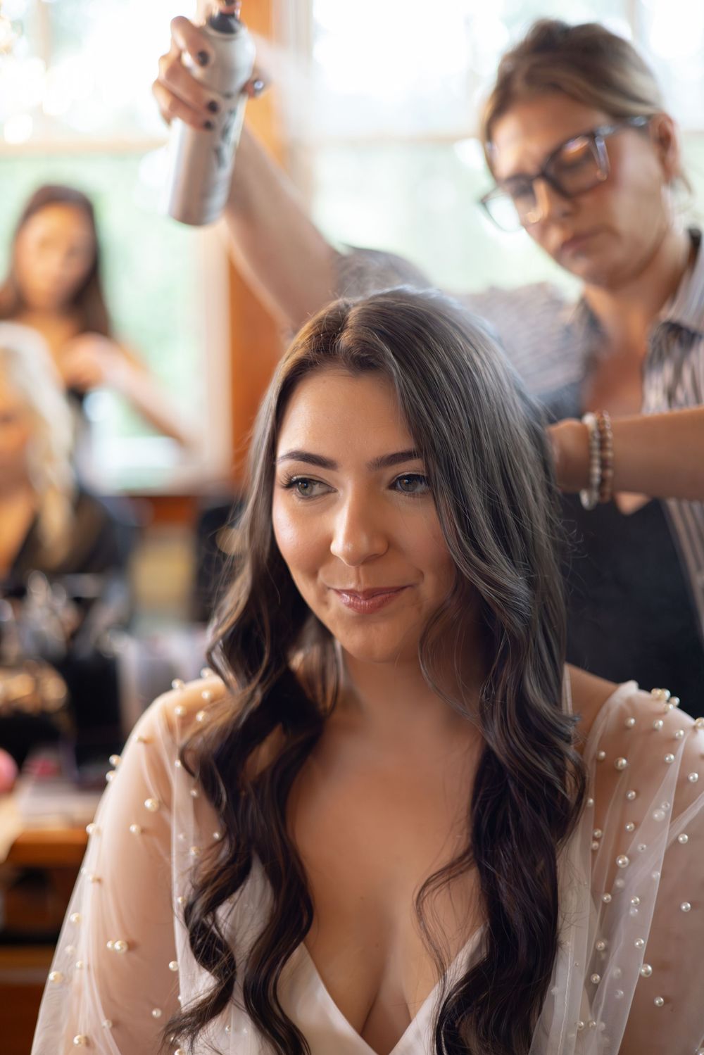 A person getting their hair styled in a bridal preparation setting with soft natural lighting.