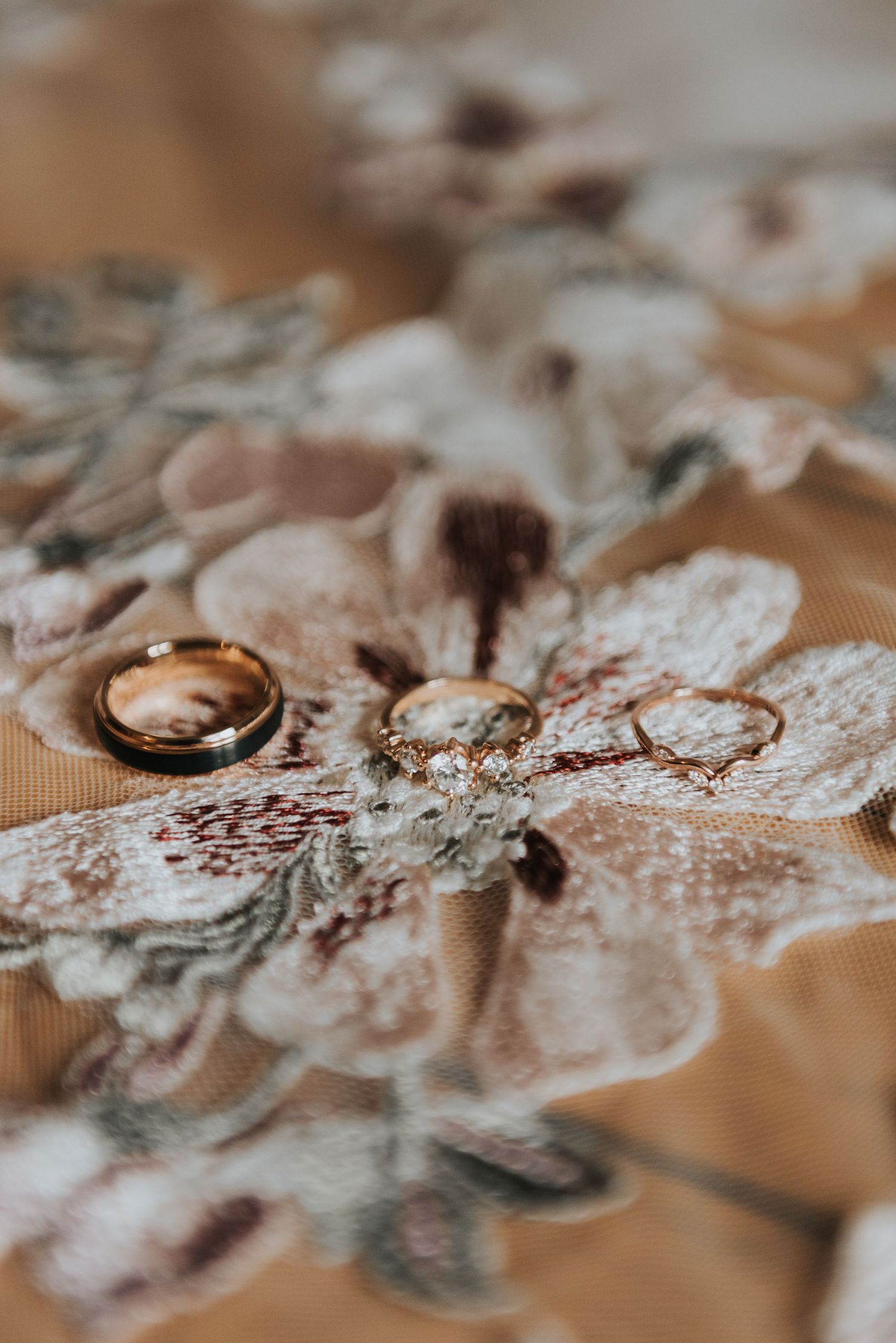 Wedding rings rest delicately on white lace fabric with a soft brown background in an artistic macro shot.