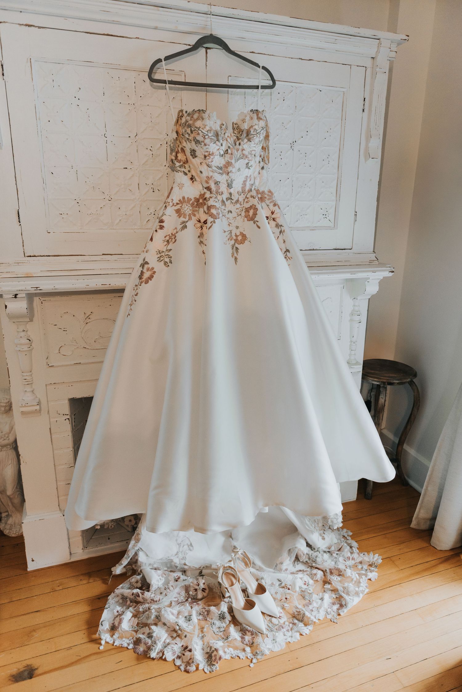 Close-up views of an elegant white wedding dress with intricate floral appliques displayed on a wooden floor.