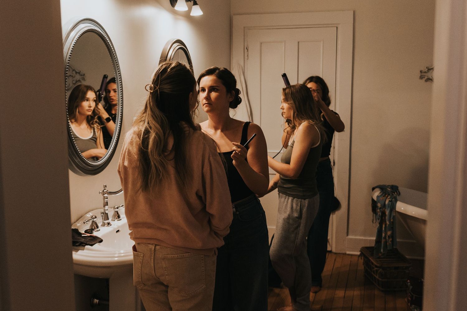 A group of people gather in a dimly lit bathroom space getting ready together.