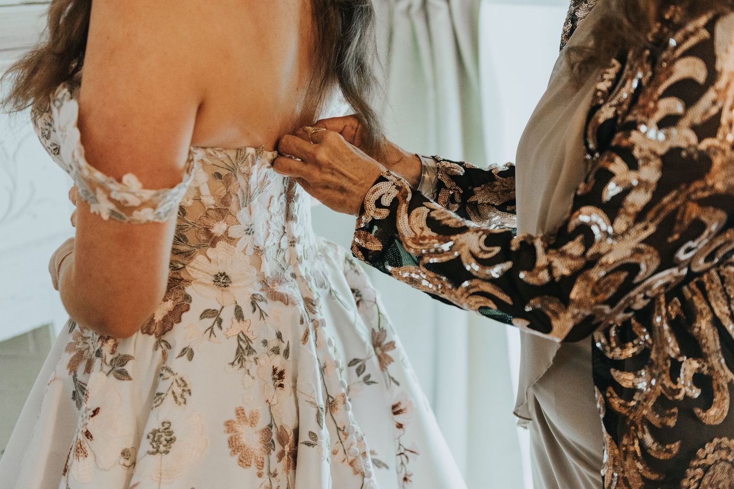 Woman in floral print dress stands in sunlit room with white curtains and decorative details.