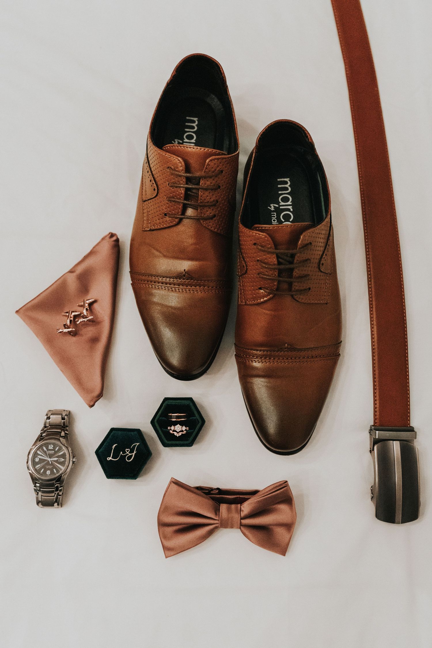Brown leather dress shoes and accessories including bow ties, belt, and watch arranged on white background.