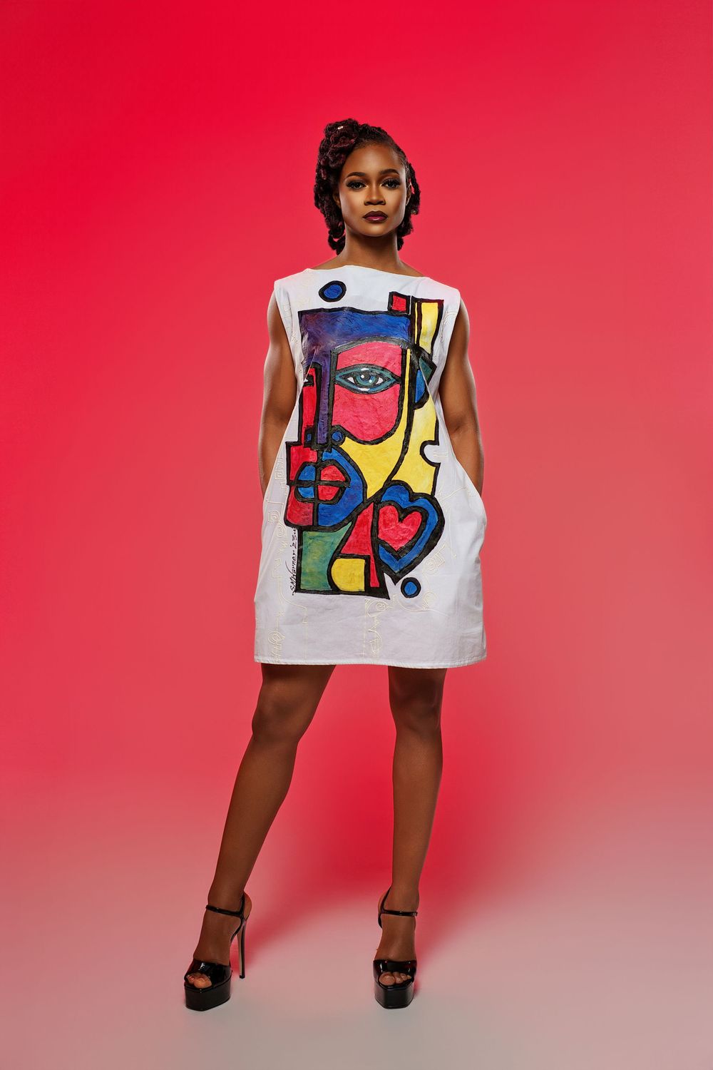 Modern art-inspired white dress with colorful geometric patterns against vibrant red background.