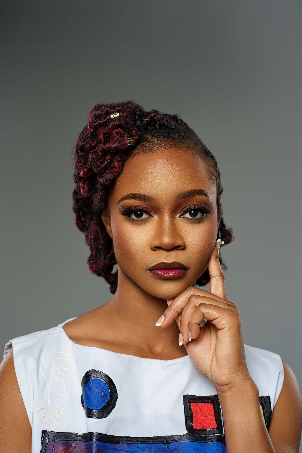 Professional beauty portrait with burgundy braided hair and white top featuring colorful artistic details.