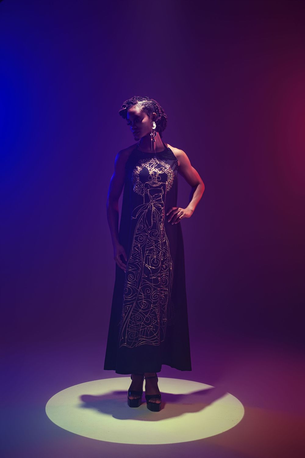 Dramatic spotlight illuminates a figure in a dark dress standing on a circular platform against a purple background.