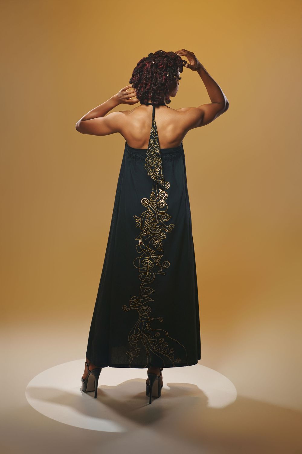 Dramatic fashion poses showcasing flowing black dress with metallic details on white platform.