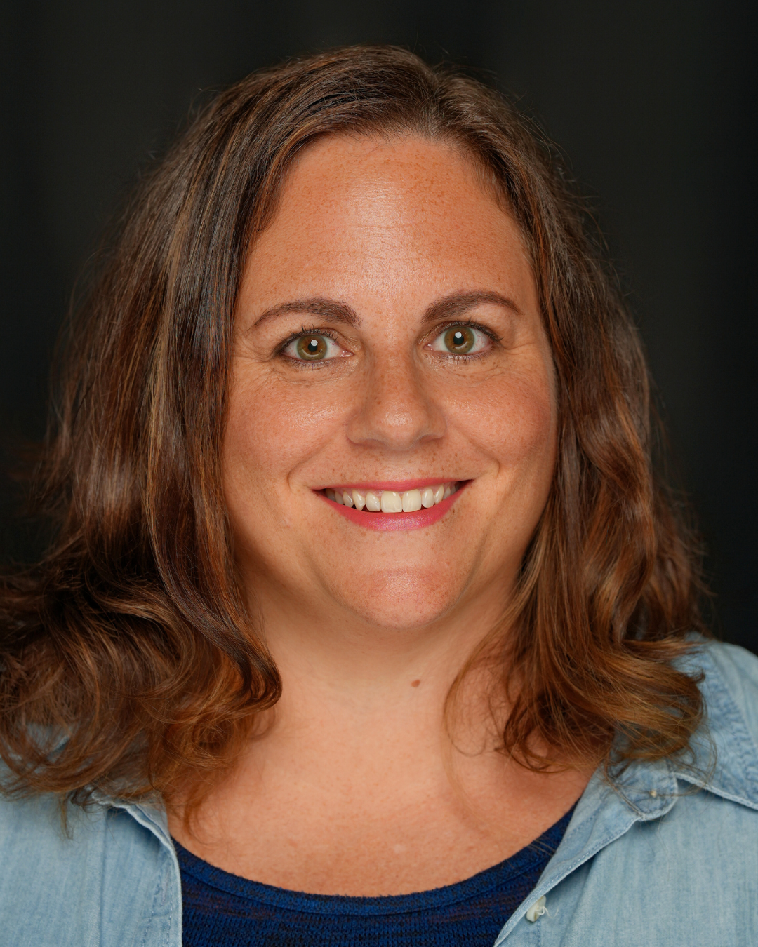 A close-up portrait of someone with long, curly dark hair against a black background.