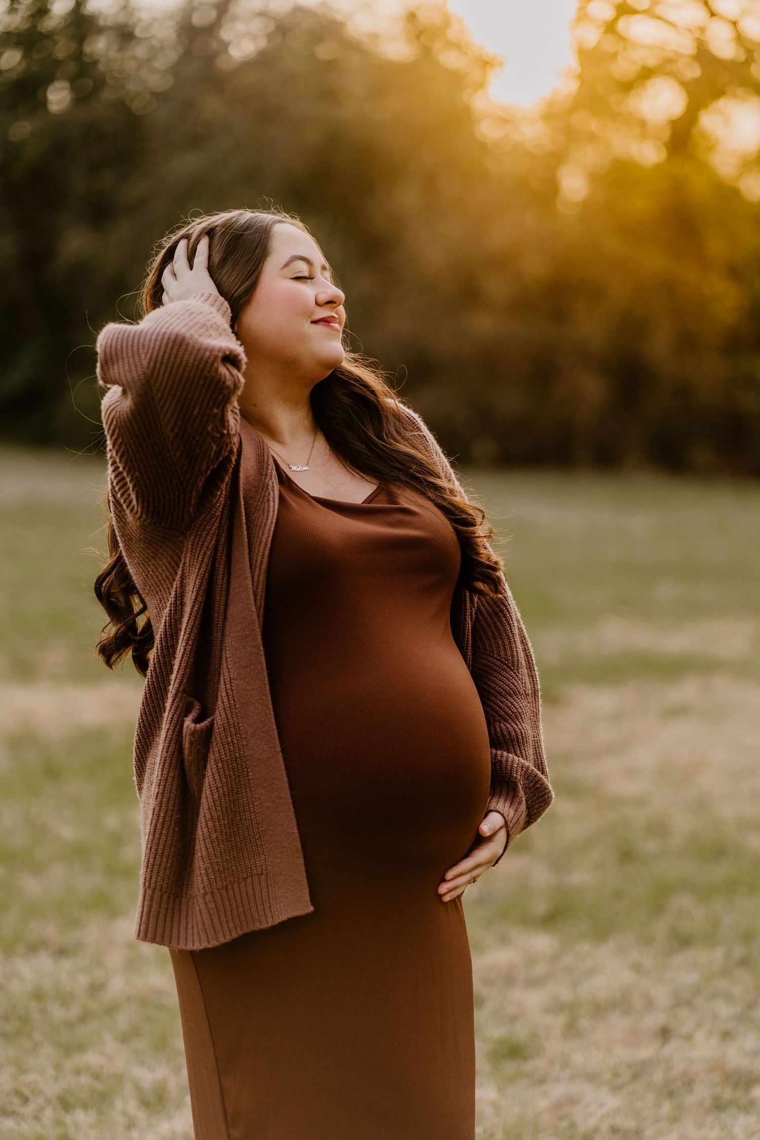 Woman in brown sweater poses expressively in field during golden hour portrait session.