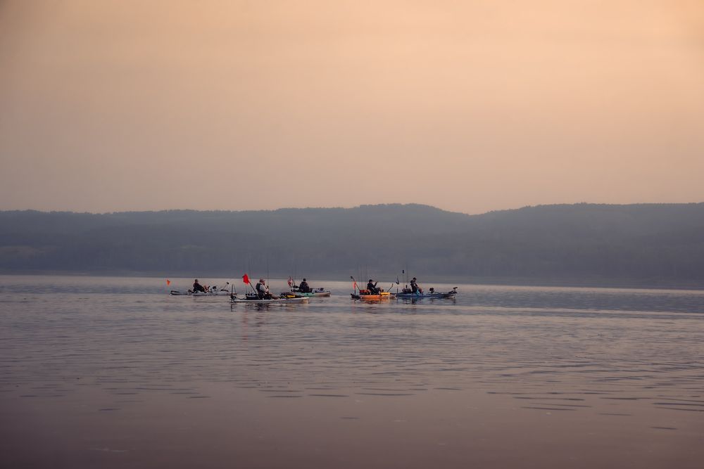 Kayakers paddle across calm waters at sunset with mountains silhouetted in the background.