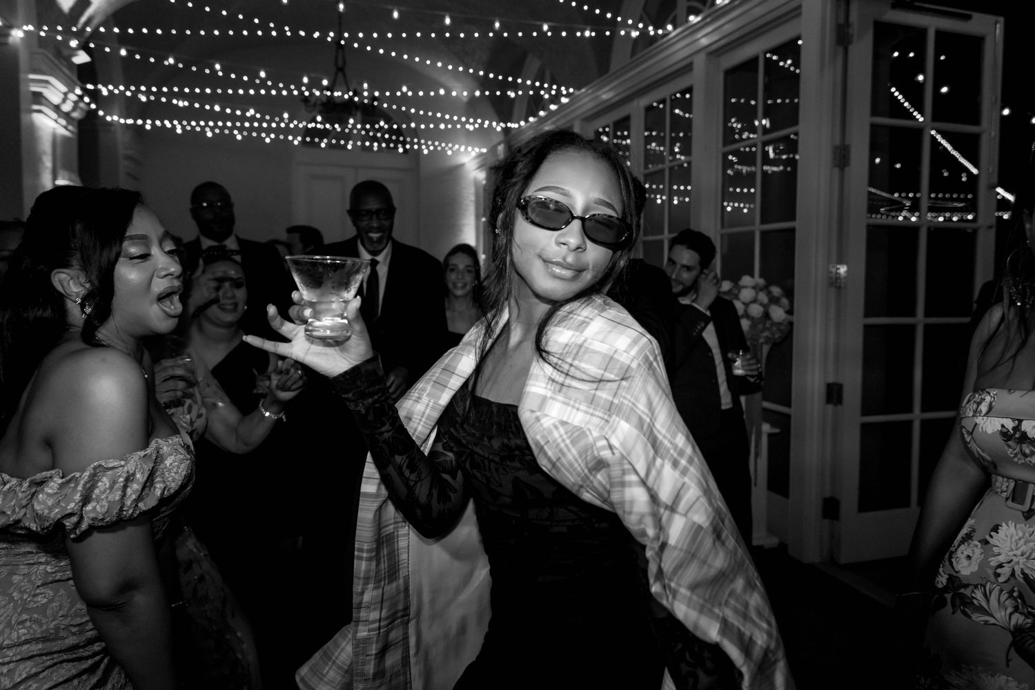 A crowded party scene with string lights overhead and people dancing in a dimly lit indoor space.