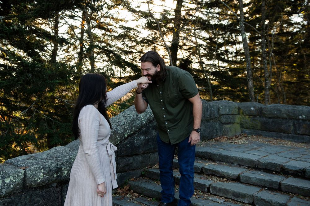 A couple shares a playful moment on stone steps in a forest during golden hour.
