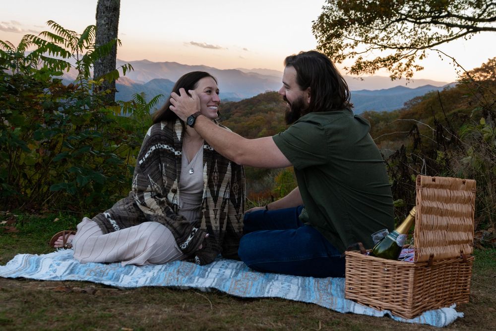 Romantic picnic setup with blanket and basket against scenic mountain backdrop at golden hour.
