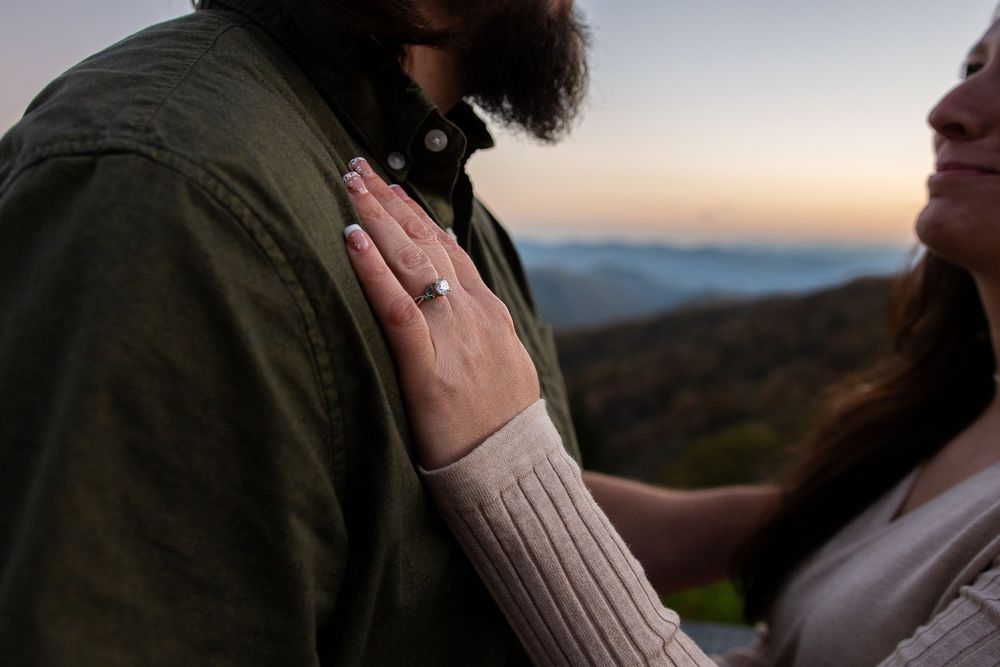 A couple embraces during sunset in a mountainous landscape wearing casual outdoor clothing.