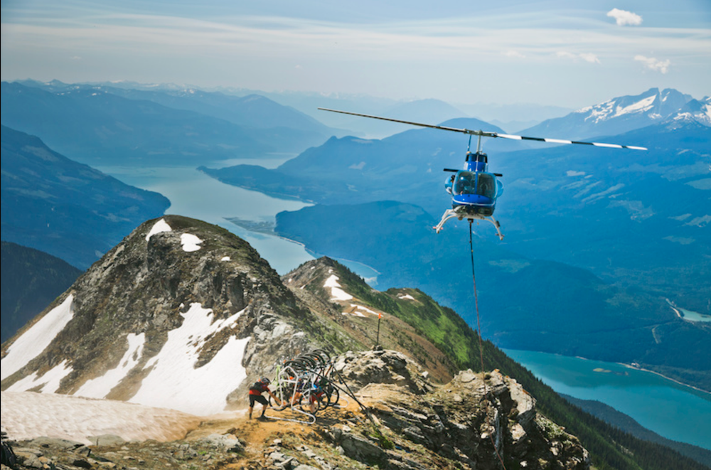 A helicopter drops passengers off on a mountain top in Revelstoke, BC with views over the surrounding mountains and lakes