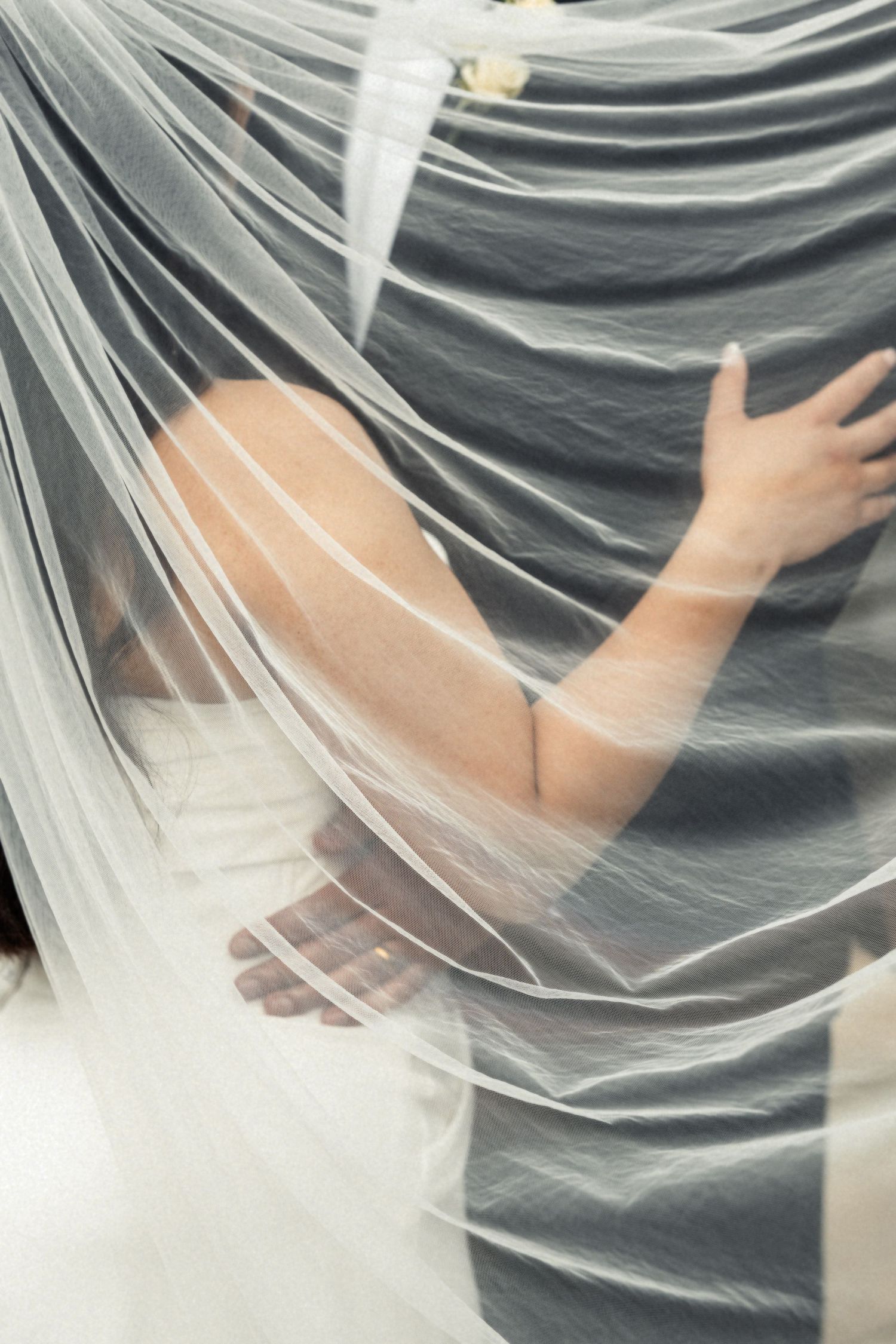 A person's hand reaches through delicate white sheer fabric creating an ethereal and artistic visual effect.