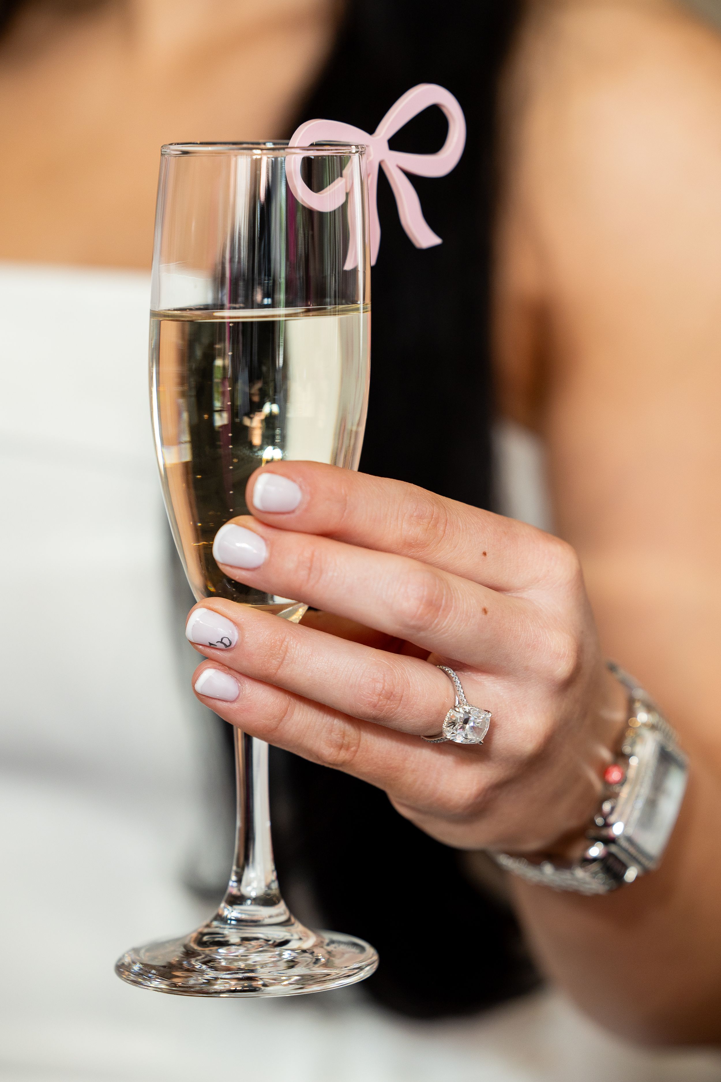Close-up of champagne glasses with pink ribbons and manicured hands holding stemware.