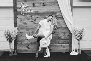 Wedding party poses against rustic wooden wall with white decor elements.