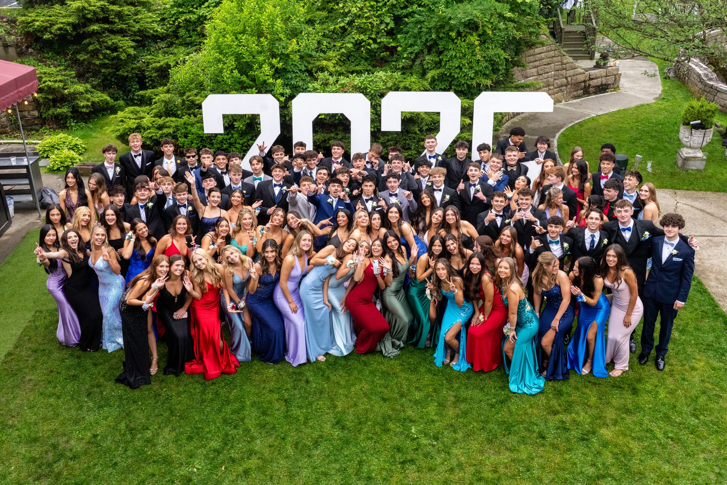 Large graduation class poses together outdoors in colorful formal attire.