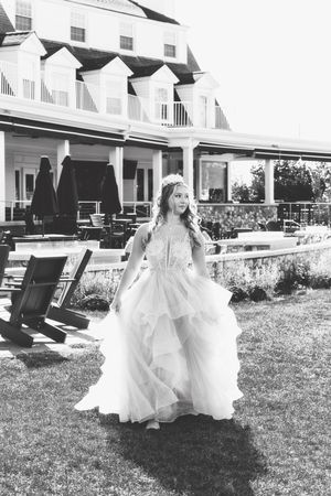 Bride in flowing white gown twirls on grassy lawn with colonial style building in background.