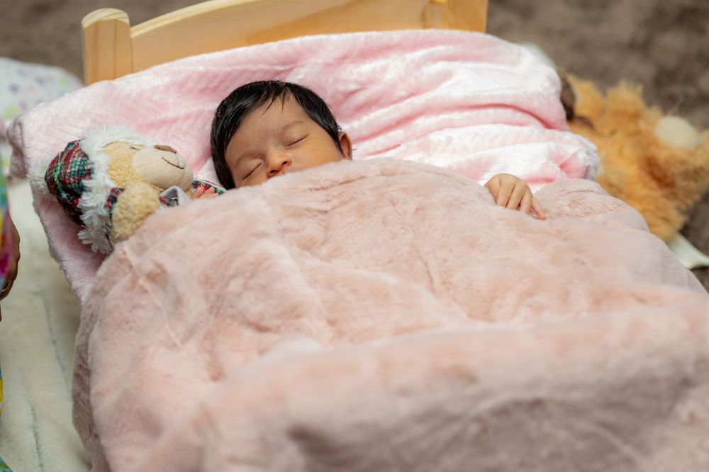 A sleeping child nestled under a soft pink blanket with a plush toy companion.