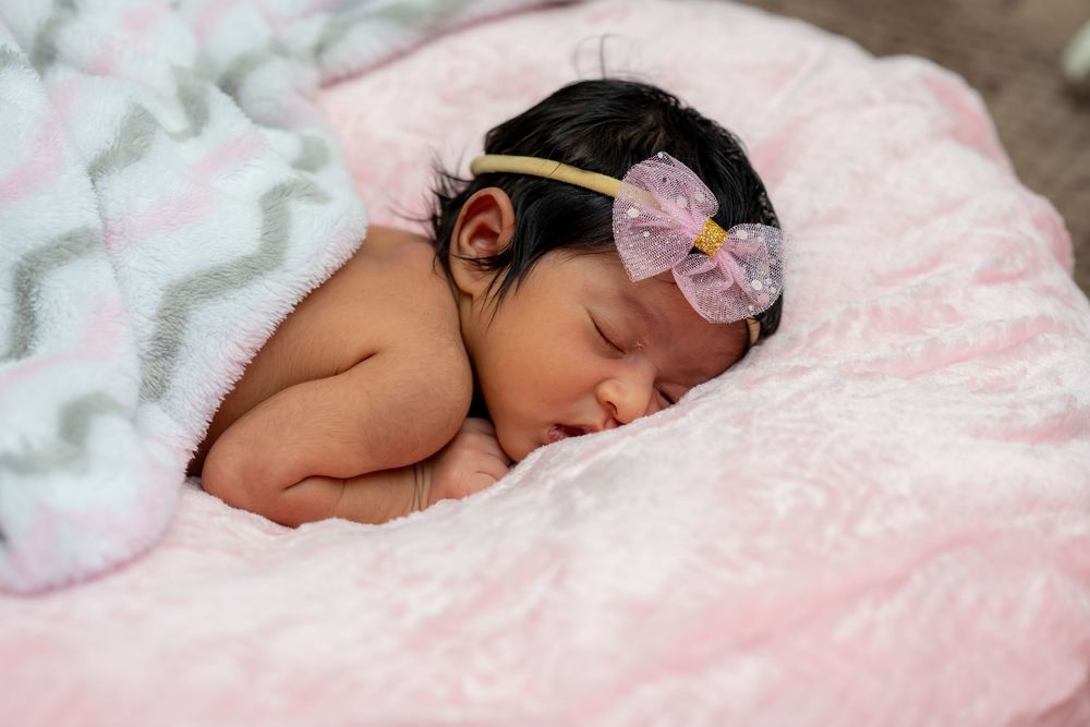Sleeping baby in pink bedding rests peacefully with a delicate floral headband.