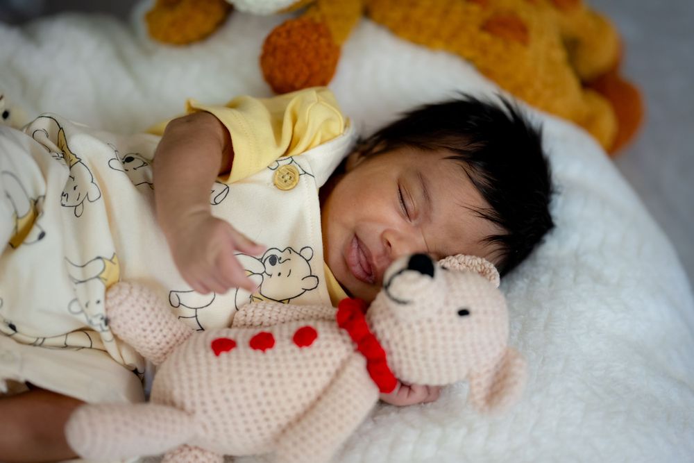 A sleeping baby lies peacefully on white bedding while holding a plush toy.