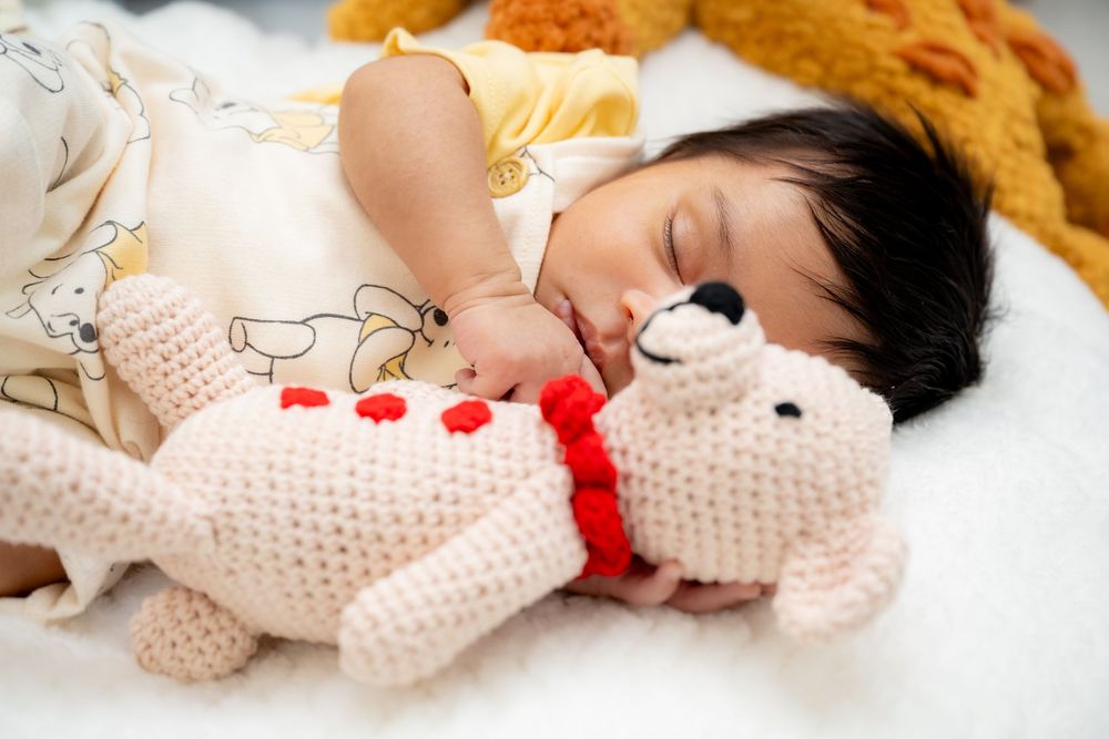 A sleeping figure in a white polka dot outfit with a red bow rests peacefully on white bedding.