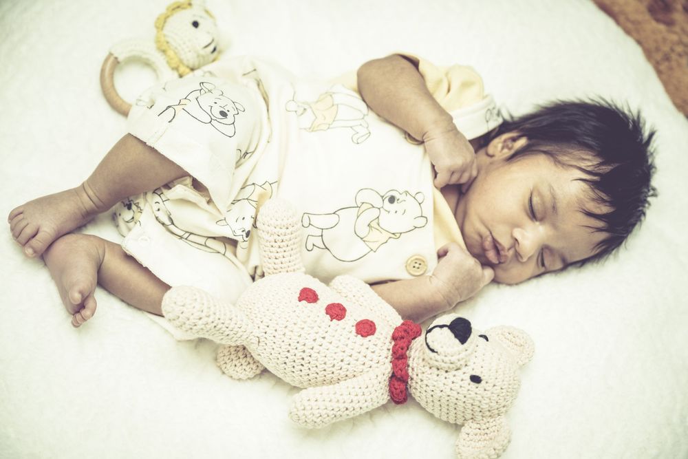 A sleeping baby wearing a white polka dot outfit with red accents lies peacefully on white bedding.