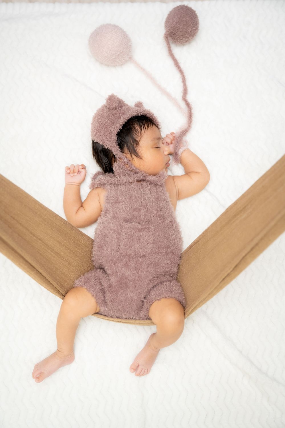 Sleeping baby wearing a fuzzy brown onesie lies on white bedding with wooden accents in a sequence of four photos.