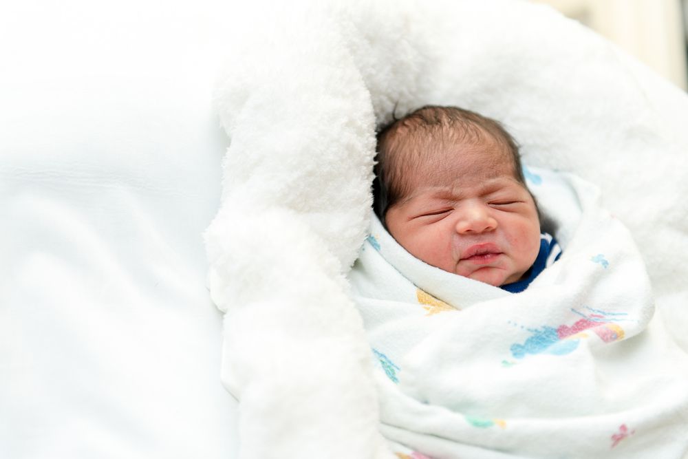 A newborn baby wrapped in a soft white blanket with delicate blue and pink patterns.