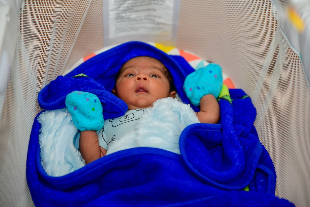 A baby wearing a bright blue swaddle blanket lies on a white surface while sleeping peacefully.