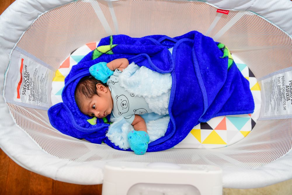 A sleeping baby lies in a blue blanket inside a white circular bassinet.