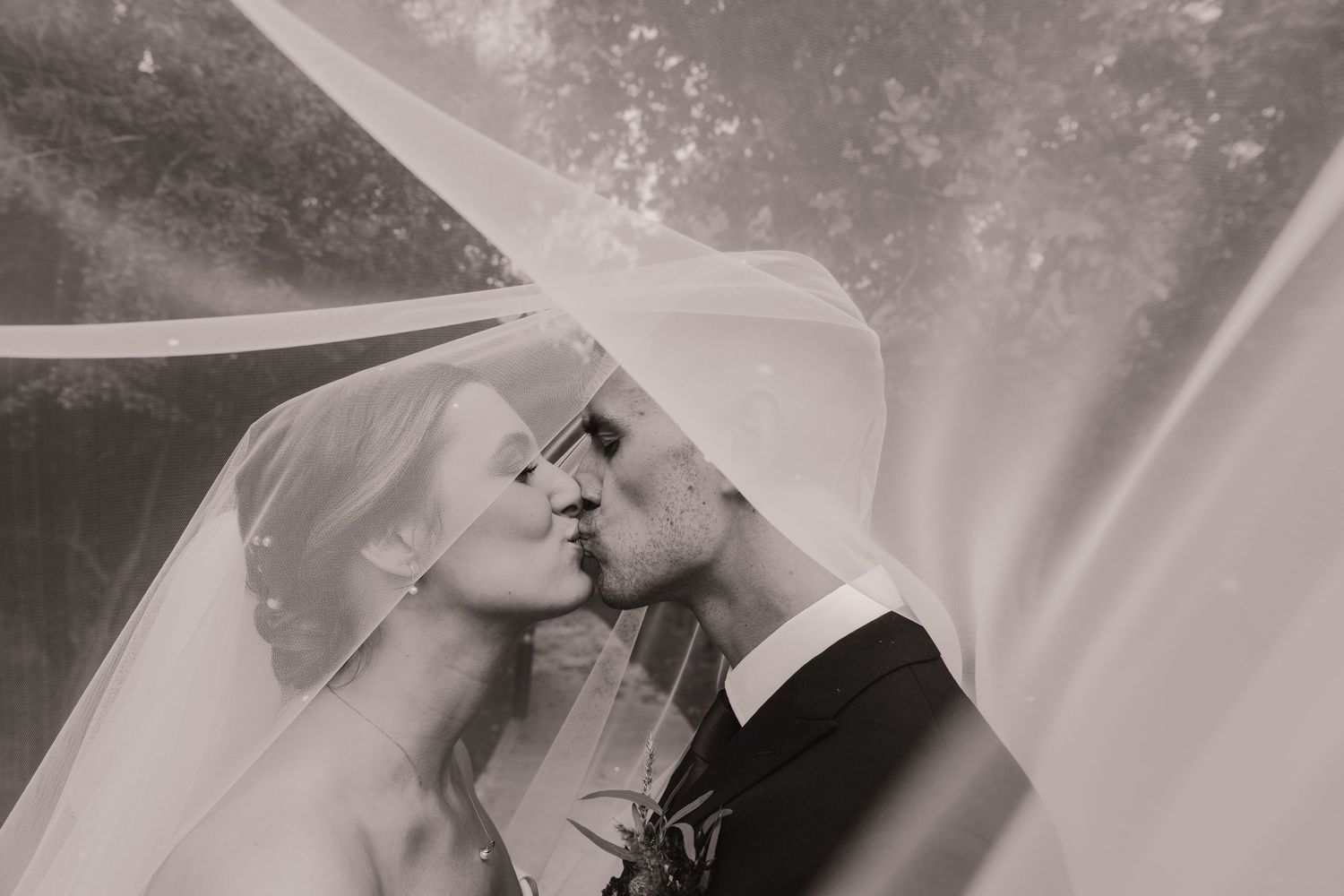 A romantic black and white wedding portrait captures a tender moment between newlyweds with flowing veil.