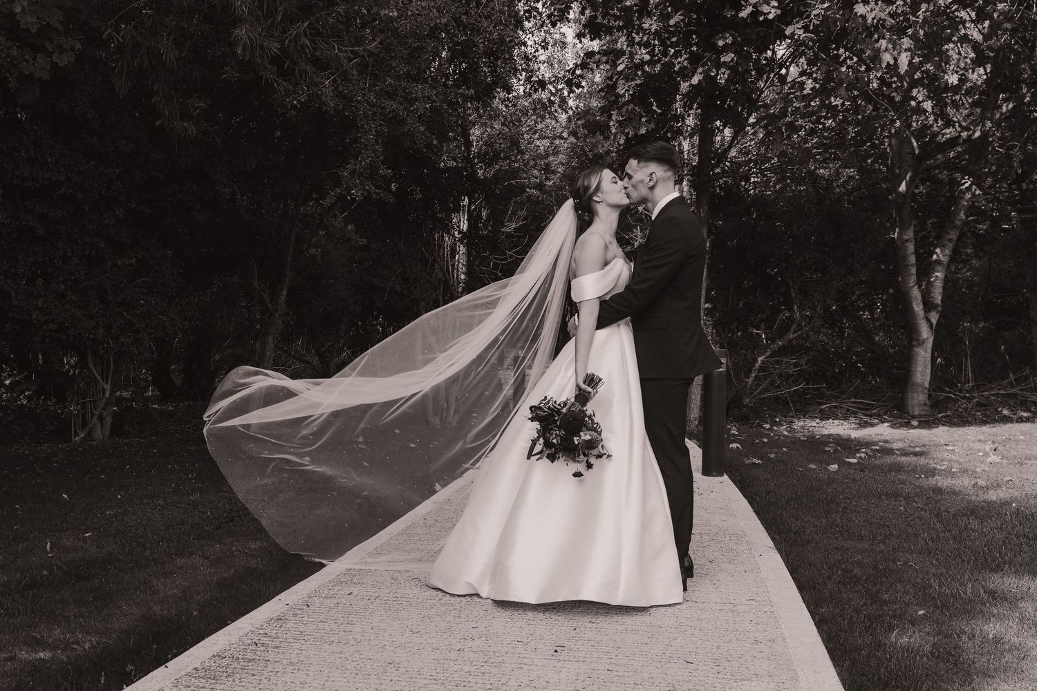 A romantic wedding couple dances together in an outdoor garden setting with flowing white dress and veil.