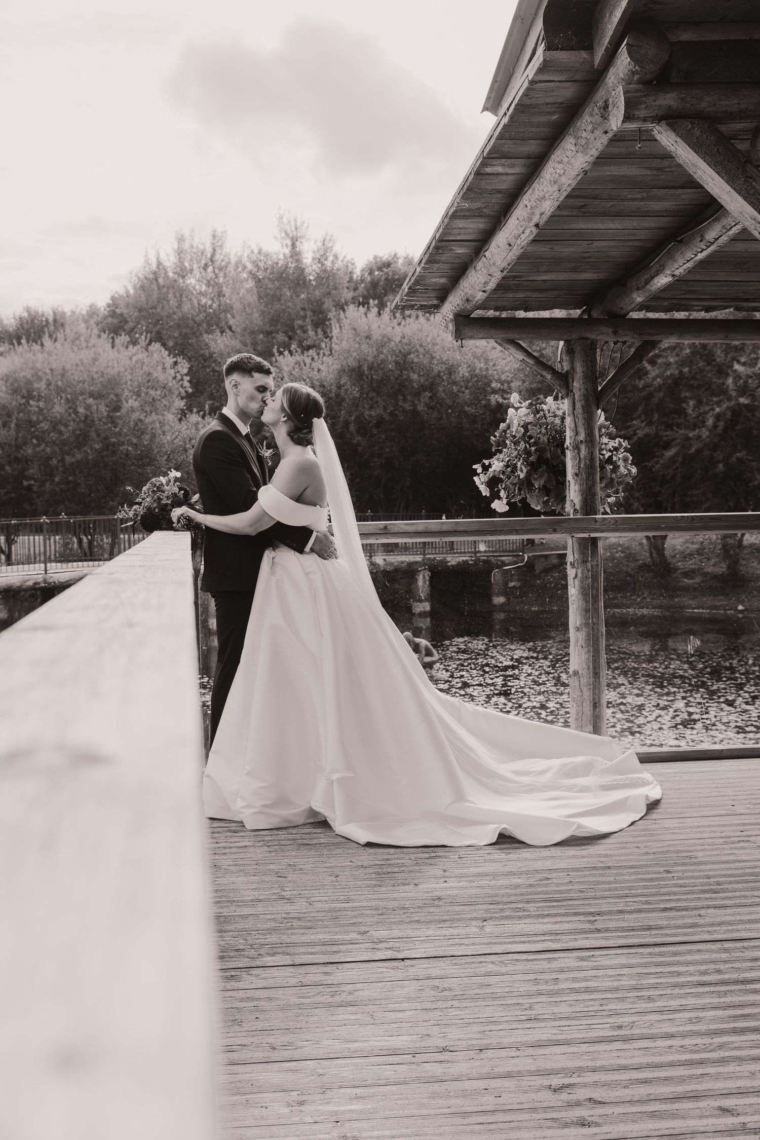 A wedding couple shares an intimate moment on a rustic wooden deck surrounded by nature.