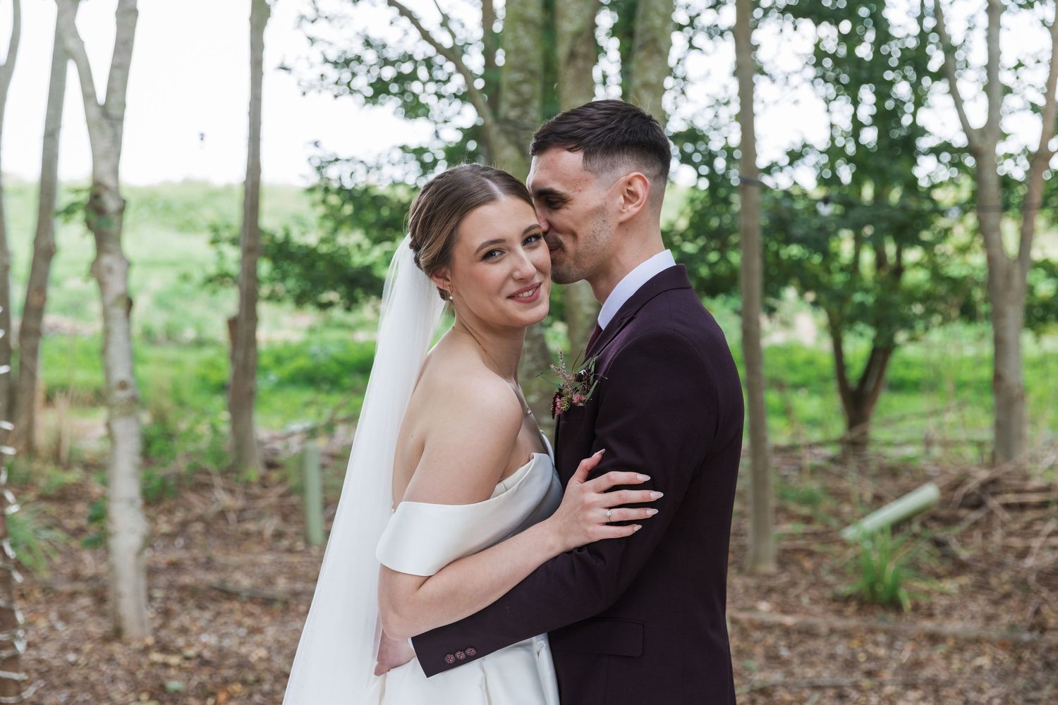 A romantic couple embraces in a wooded outdoor setting during their wedding photo session.