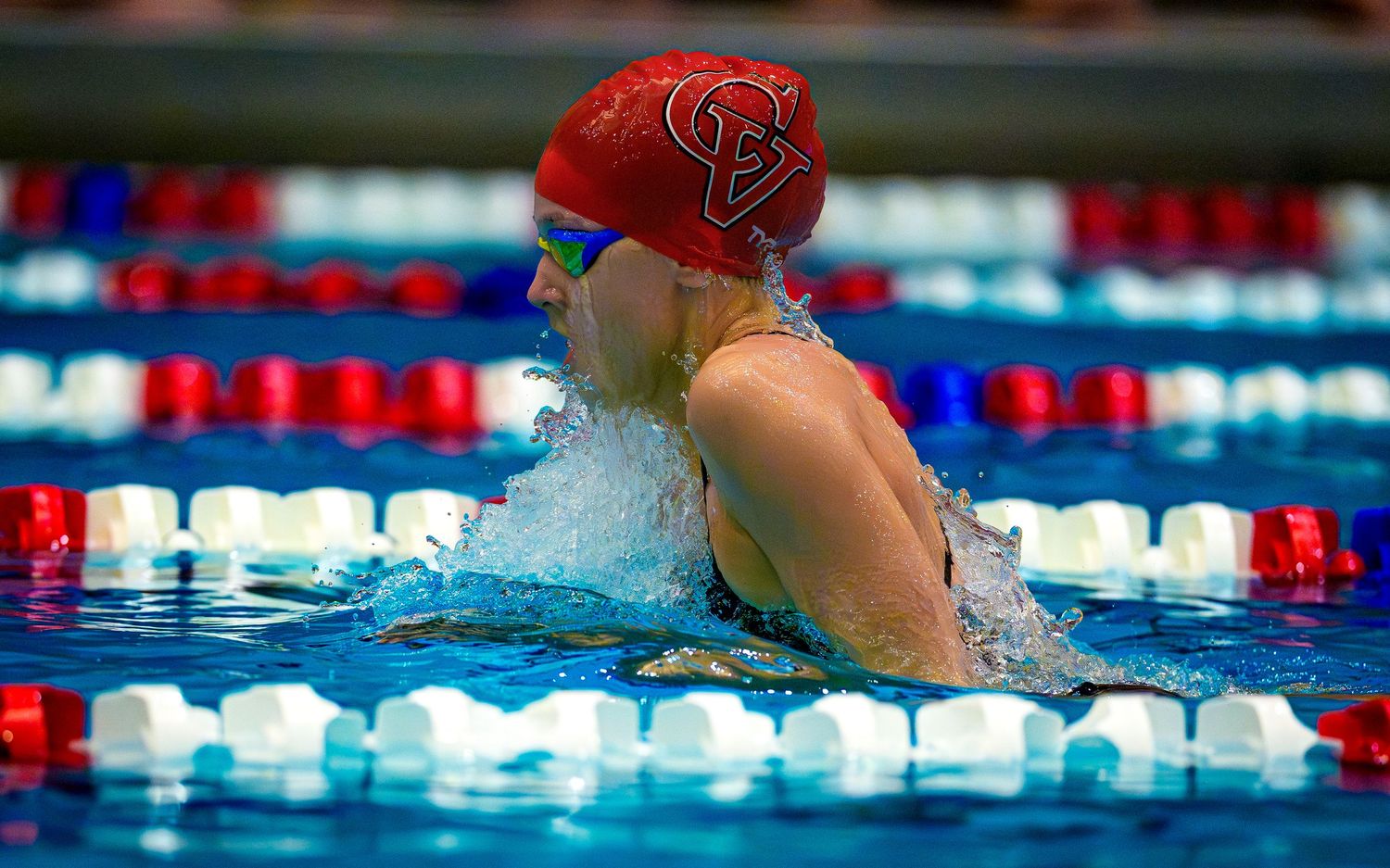 High school swimmer in red cap competing in breaststroke event, action photo during meet, team photo day by SportsFox Photography
