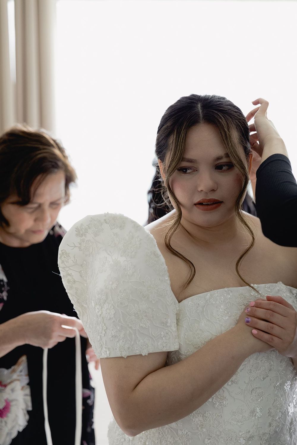 Bride in white lace wedding dress gets final adjustments made to her gown and hair before the ceremony.